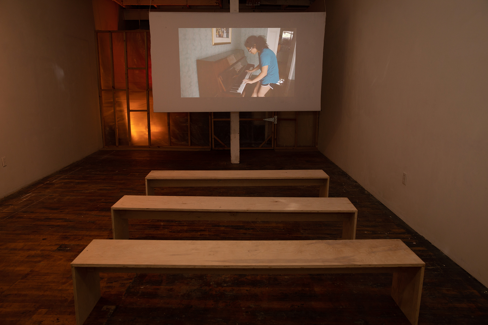 A projection screen with three wooden benches for seating in front in a room with warm lighting